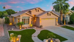 A two-story house with a garage, a well-maintained lawn, and a palm tree. - Lakefront Oasis | Infinity Edge Pool & Golf Views (Glendale)