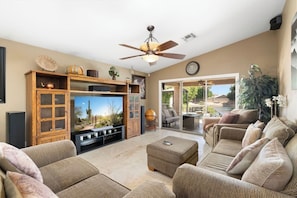 A living room with a flat-screen TV, wooden cabinets, a ceiling fan, and a sliding glass door leading to an outdoor patio. - Lakefront Oasis | Infinity Edge Pool & Golf Views (Glendale)