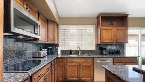 A kitchen with wooden cabinets, granite countertops, a built-in microwave, and a dishwasher. - Lakefront Oasis | Infinity Edge Pool & Golf Views (Glendale)