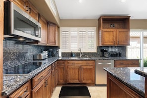 A kitchen with wooden cabinets, granite countertops, a built-in microwave, and a dishwasher. - Lakefront Oasis | Infinity Edge Pool & Golf Views (Glendale)