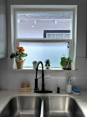 Eine Küche mit Fenster, Edelstahl-Spülen, einem Wasserhahn und Blumentöpfen auf der Fensterbank.