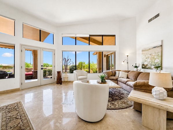 A spacious living room with a high ceiling, large windows, a sectional sofa, a white armchair, and a coffee table. - Luxury Retreat w Incredible Views! (Mesa)