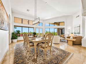 A spacious living area with a dining table, chairs, and a sofa. There are large windows offering a view of the outdoors. - Luxury Retreat w Incredible Views! (Mesa)
