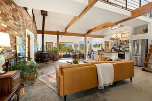 A spacious living area with a sofa, wooden beams, a brick wall, and a kitchen with modern appliances. - Amazing views 15 minutes from Fayetteville square! (fayetteville)