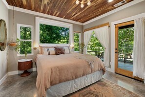 A bedroom with a large bed, a wooden ceiling, and a view of trees through the windows. - Amazing views 15 minutes from Fayetteville square! (fayetteville)