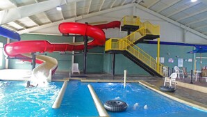 An indoor swimming pool with two slides, a yellow staircase, and a tire float.