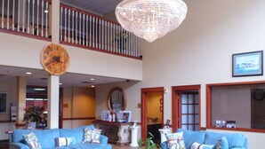 A spacious lobby with two blue sofas, a large chandelier, a patterned rug, and a high ceiling with a balcony.