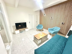 Ein modernes Wohnzimmer mit Flachbildfernseher, zwei blauen Sesseln, einer Couch und einer Holzvertäfelung.