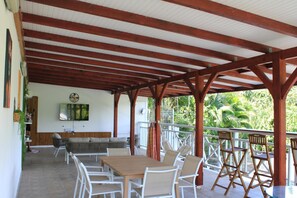 Ein überdachter Patio-Bereich mit Holztisch und Stühlen, einer Couch und einem an der Wand befestigten Fernseher.