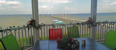 Een overdekt terras met een tafel en stoelen, met uitzicht op een waterpartij en een steiger.