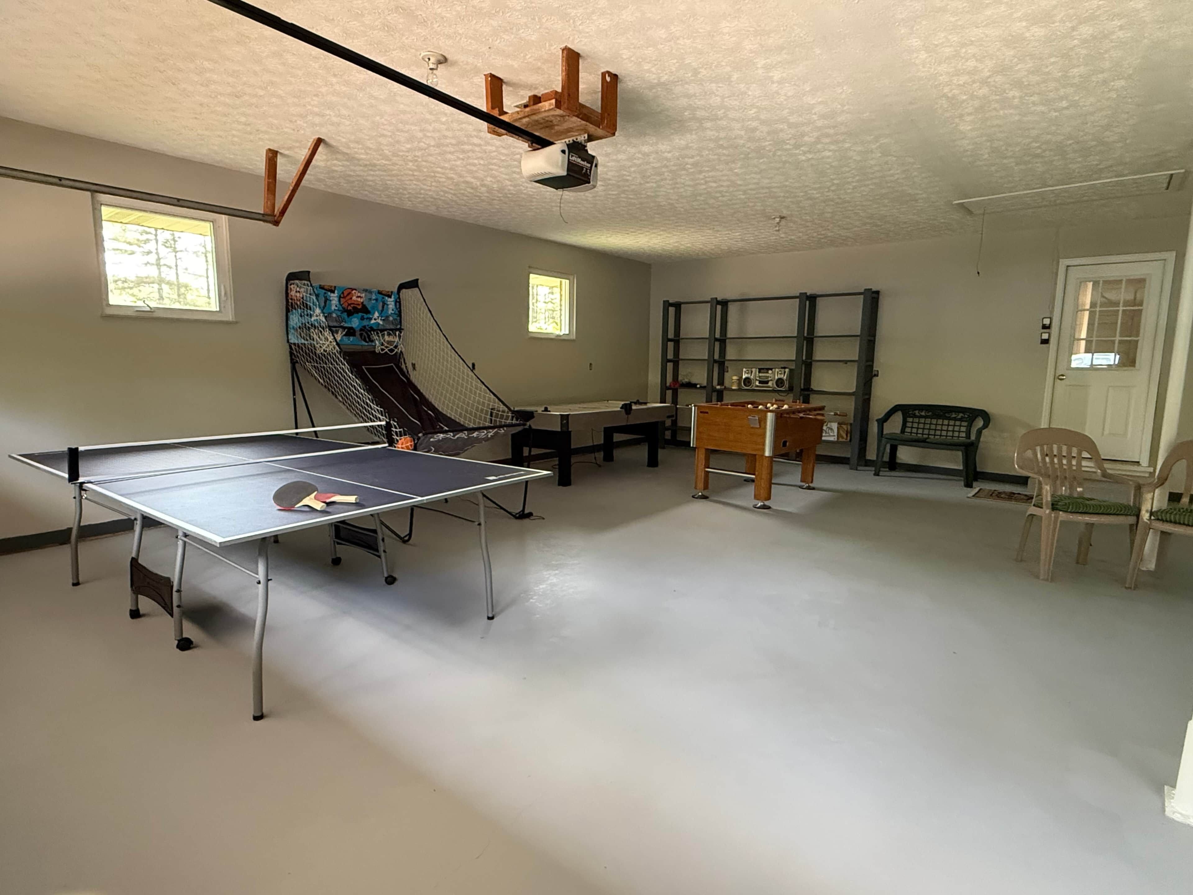 A room with a ping pong table, a pool table, a sofa, and a door.