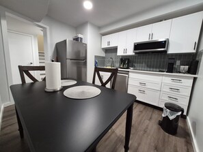 A modern kitchen with white cabinets, a black countertop, a stainless steel refrigerator, a microwave, and a coffee maker. - Lower Suite with Separate Entrance in Northridge, Grande Prairie (Grande Prairie)