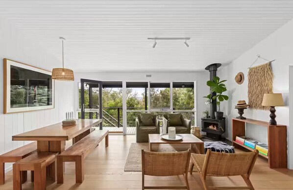 A spacious living area with a wooden table, benches, a sofa, and a fireplace. - Coastal Sanctuary (Anglesea)