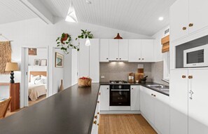 A modern kitchen with white cabinetry, a central island, a stove, and a microwave. - Coastal Sanctuary (Anglesea)