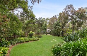 A well-maintained garden with a variety of plants and trees, a grassy lawn, and a house in the background. - Coastal Sanctuary (Anglesea)