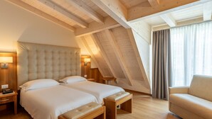 A room with two beds, a bench, a chair, and a window with curtains. - Royal Suite (Garda)
