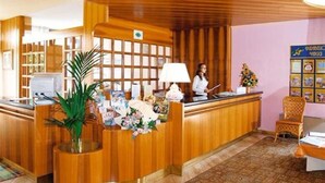 A reception desk with a wooden finish, a potted plant, and a floral arrangement. - Royal Suite (Garda)