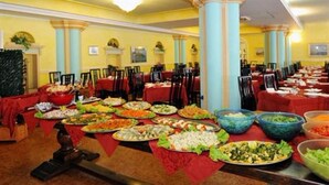 A banquet hall with multiple tables covered in various dishes, a high ceiling with columns, and a warm color scheme. - Royal Suite (Garda)