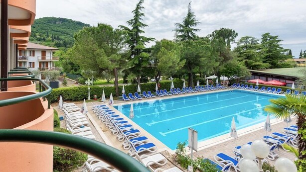 A swimming pool with lounge chairs, surrounded by trees and buildings. - Royal Suite (Garda)