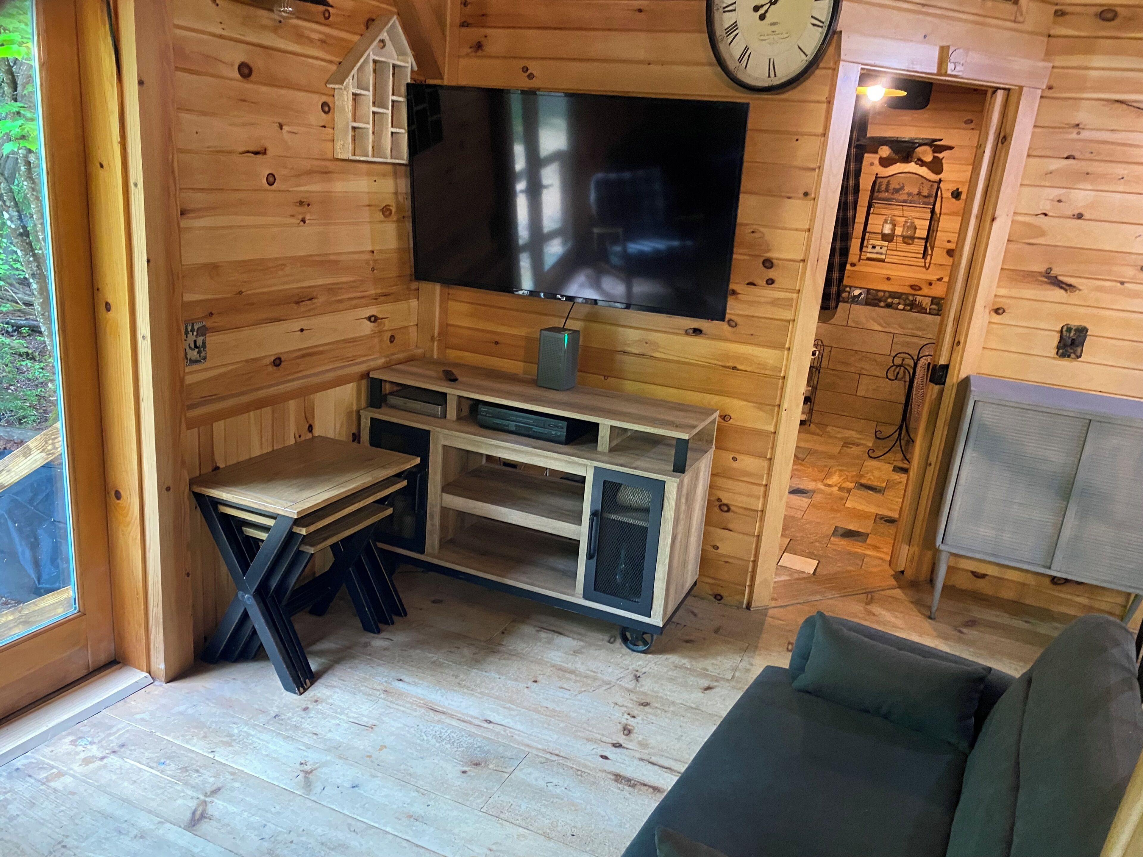 L’intérieur d’un chalet en bois, avec un téléviseur, une petite table, un canapé et une horloge au mur.
