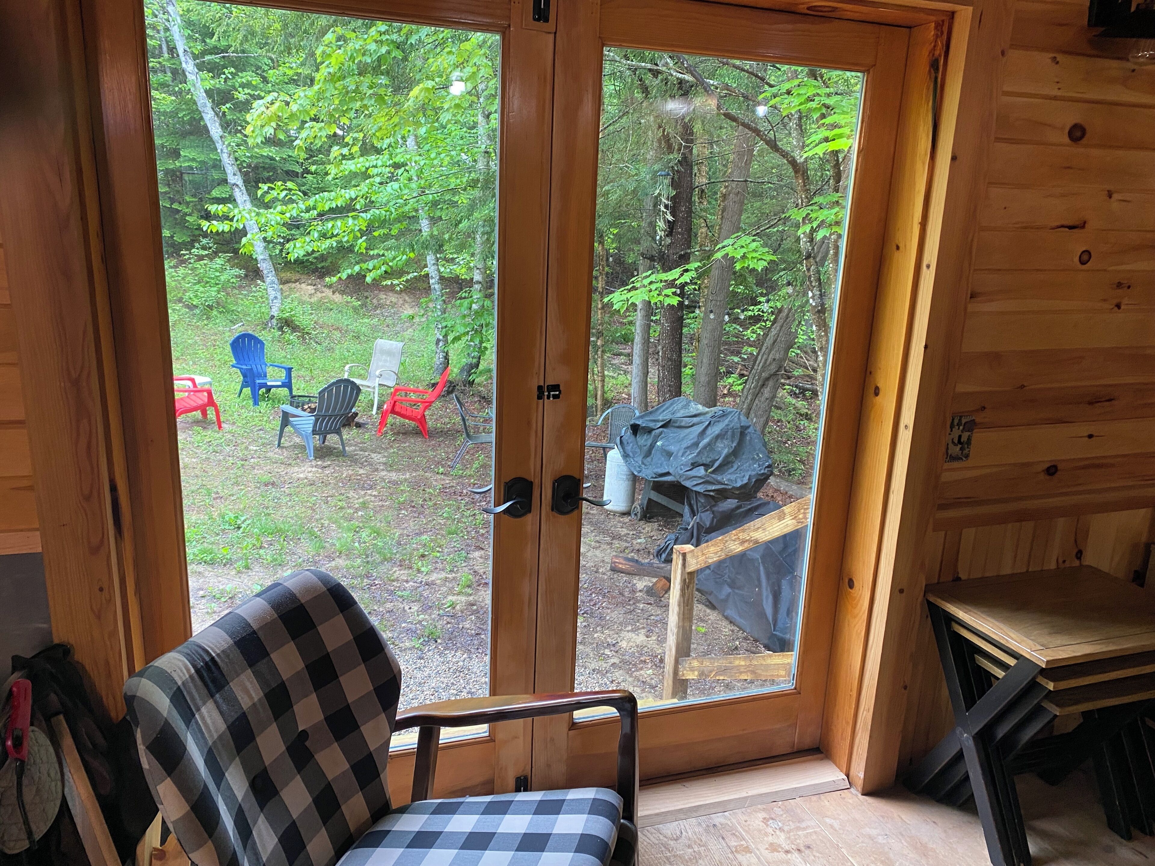 Une cabane en bois avec une porte en verre donnant sur un espace extérieur aménagé avec des chaises et une table.