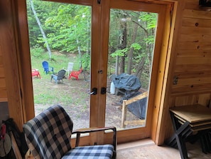 A wooden cabin with a glass door leading to an outdoor area with chairs and a table.