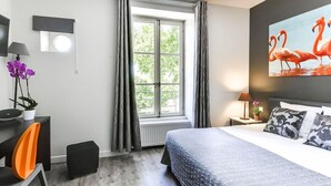 A bedroom with a bed, a desk, a chair, a window with curtains, a painting, and a potted plant. - Hotel De L'estelou (Sommieres)