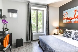 Quarto com cama, escrivaninha, cadeira, janela com cortinas, quadro e planta em vaso.