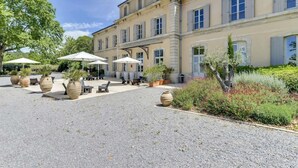 A large building with multiple windows and a courtyard with outdoor seating and planters. - Hotel De L'estelou (Sommieres)