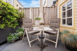 Une terrasse extérieure avec deux chaises, une table, des plantes en pot et une clôture en bois.