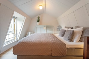 Ein Schlafzimmer mit einem Bett, einer Zimmerpflanze, einem Ventilator und einem Fenster.