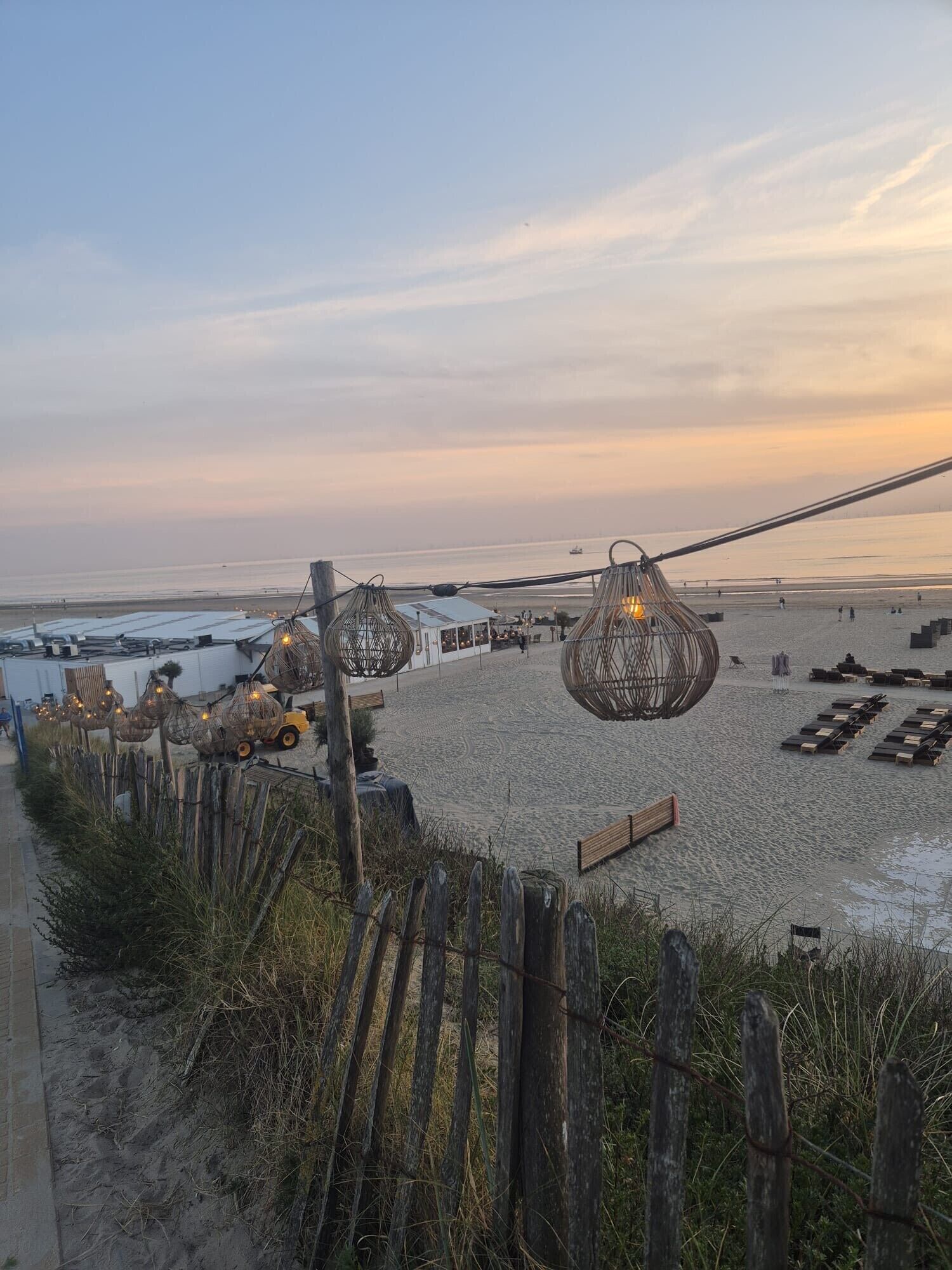 A beachside area with a sandy beach, wooden fence, and decorative hanging lights.