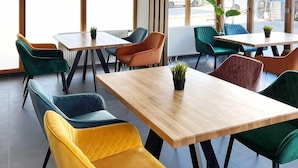 Un espace de restauration moderne, doté de plusieurs tables et chaises, de grandes fenêtres et de plantes en pot.