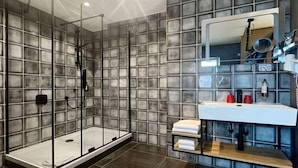 Une salle de bain moderne avec une douche à parois de verre, un grand miroir et un lavabo blanc doté d’une étagère en bois.