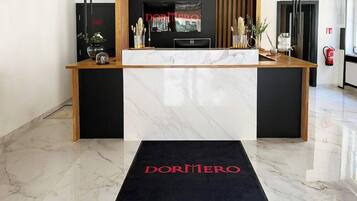 Ein Empfangstresen mit einem 'DORMERO'-Schild, einem Fernseher und einem Feuerlöscher.