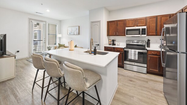 A modern kitchen with a central island, bar stools, wooden cabinets, stainless steel appliances, and a dining area with a sofa and table. - Frisco Getaway with Pool, Gym & Free Parking (Frisco)