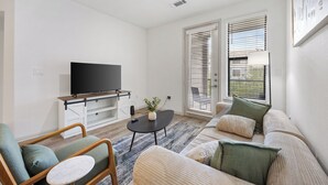 A modern living room with a flat-screen TV, a sofa, a chair, and a coffee table. - Frisco Getaway with Pool, Gym & Free Parking (Frisco)