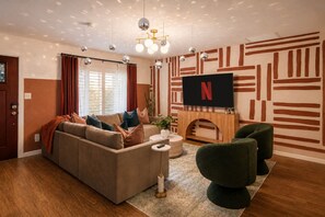 Un salon avec un canapé, un téléviseur fixé au mur, une cheminée et un mur décoré d’un motif.