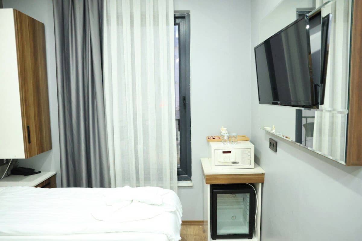 Une chambre d’hôtel avec un lit, un téléviseur fixé au mur, un petit bureau avec un ordinateur et une fenêtre avec des rideaux.