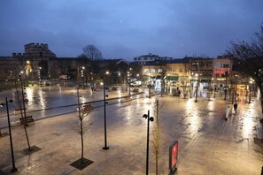Uma praça ampla com um edifício histórico, postes de luz e lojas.