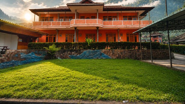 A two-story building with a balcony, surrounded by lush greenery and mountains.