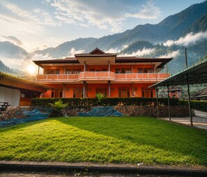 Um edifício de dois andares com varanda, rodeado por vegetação exuberante e montanhas.