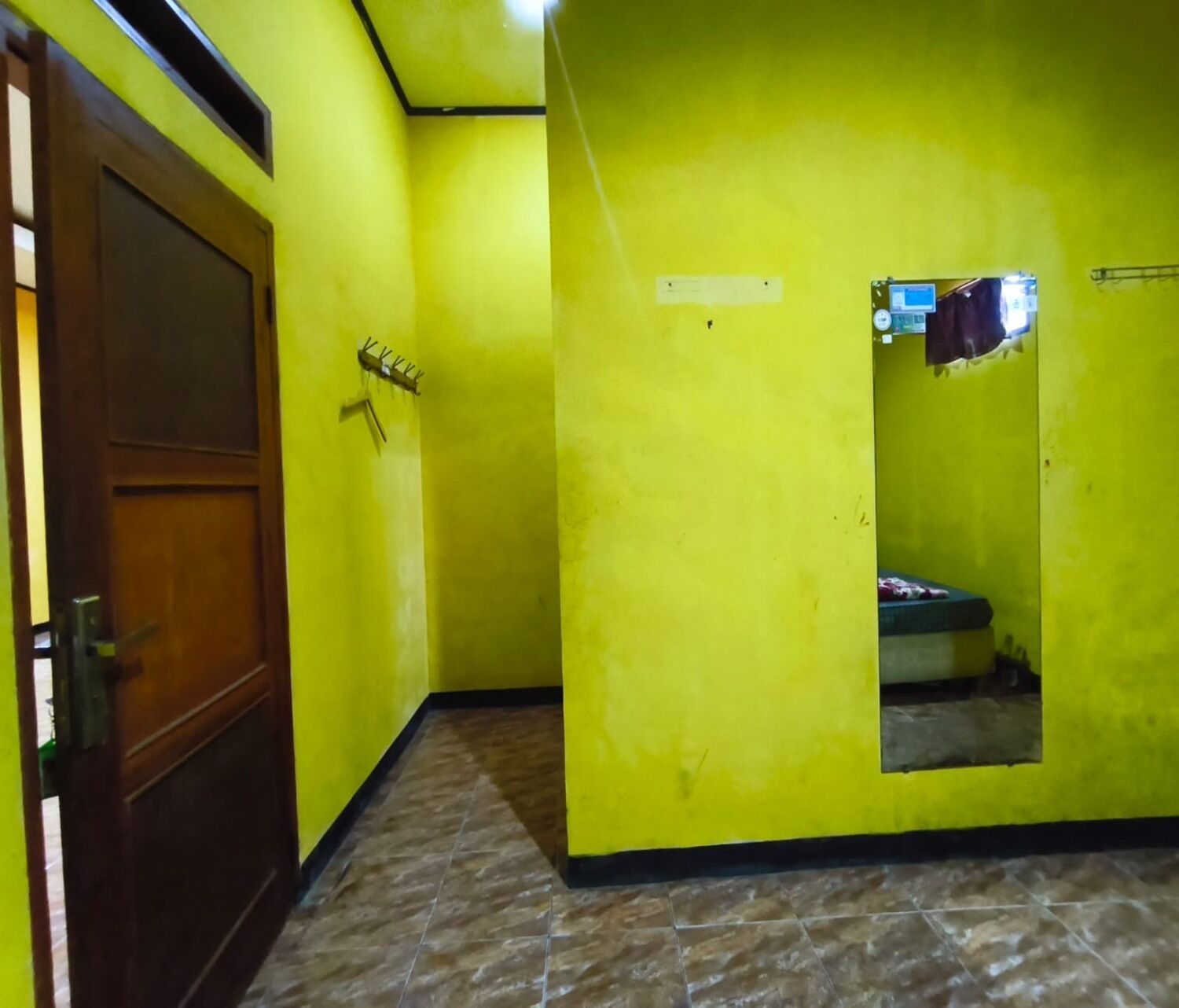 A room with yellow walls, a wooden door, a tiled floor, and a small window.