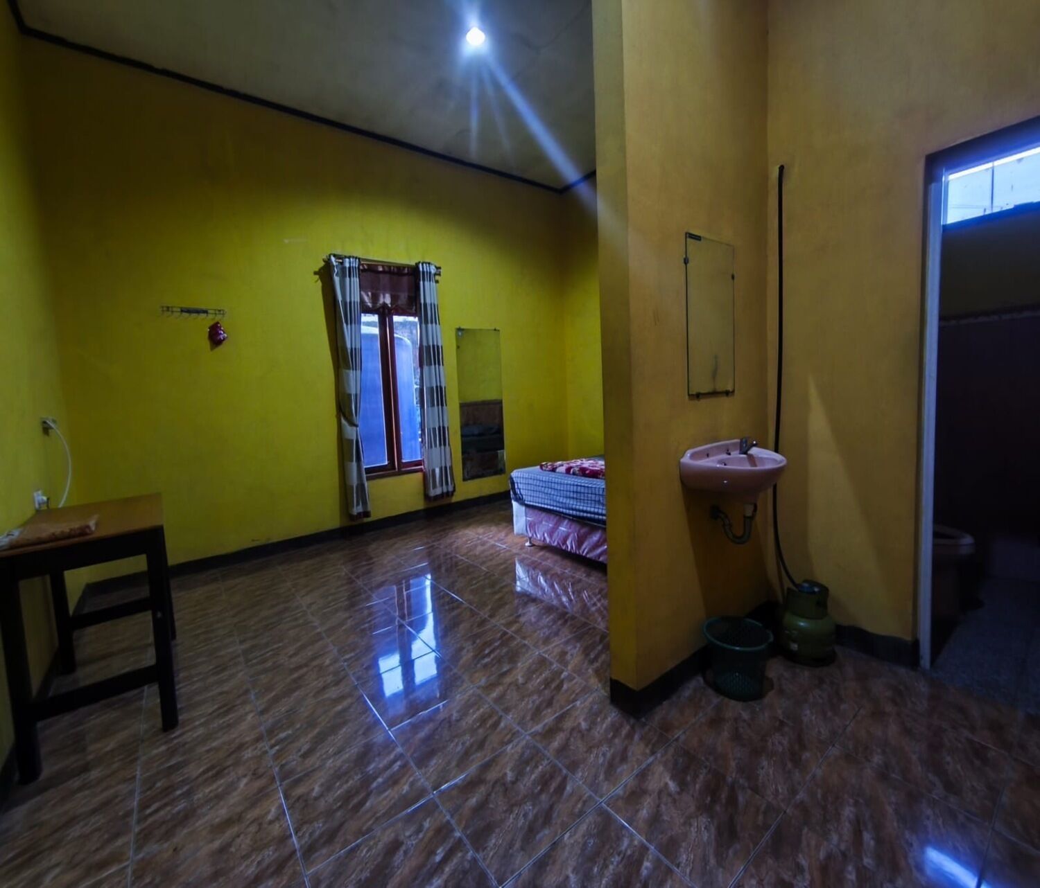 Une pièce aux murs jaunes, avec un lit, un lavabo et une fenêtre avec des rideaux.