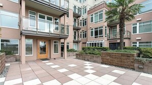 Een meerlaags woongebouw met een stoeptegels plein, balkons en een palmboom.