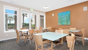 Een vergaderruimte met tafels en stoelen, grote ramen met uitzicht op palmbomen en een schilderij aan de muur.