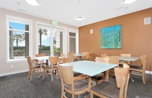 A conference room with tables and chairs, large windows with views of palm trees, and a painting on the wall.