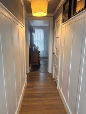 Ein Flur mit Holzboden, weißen Wänden und einer Tür zu einem Badezimmer.
