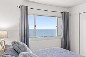 Ein Schlafzimmer mit großem Fenster, einem Bett, einer Lampe und Meerblick.