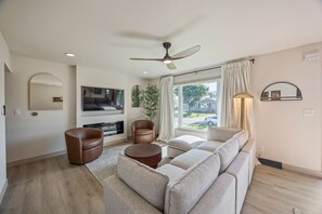Ein modernes Wohnzimmer mit einer Couch, Sesseln, einem Fernseher und einem Deckenventilator.